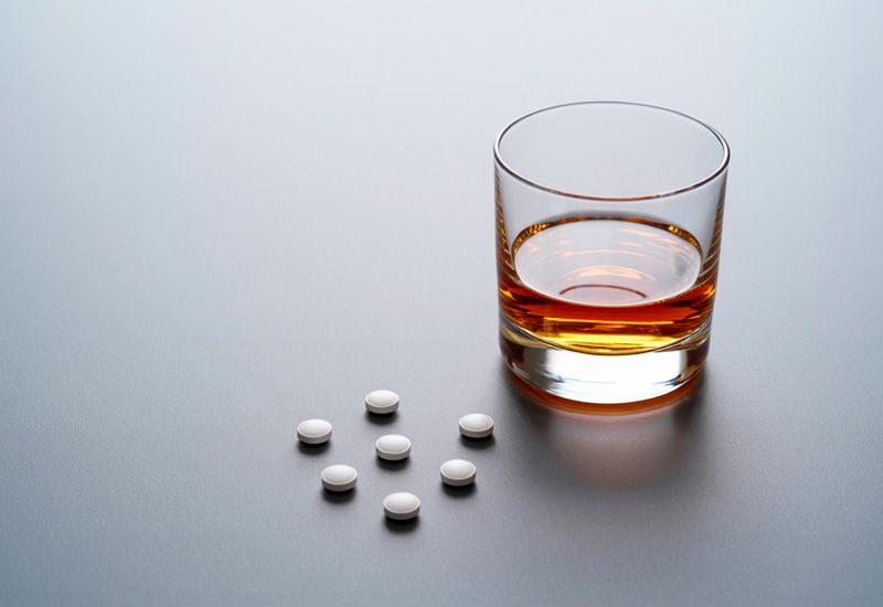 Стакан с янтарным алкоголем и несколько белых таблеток лежат на гладкой серой поверхности